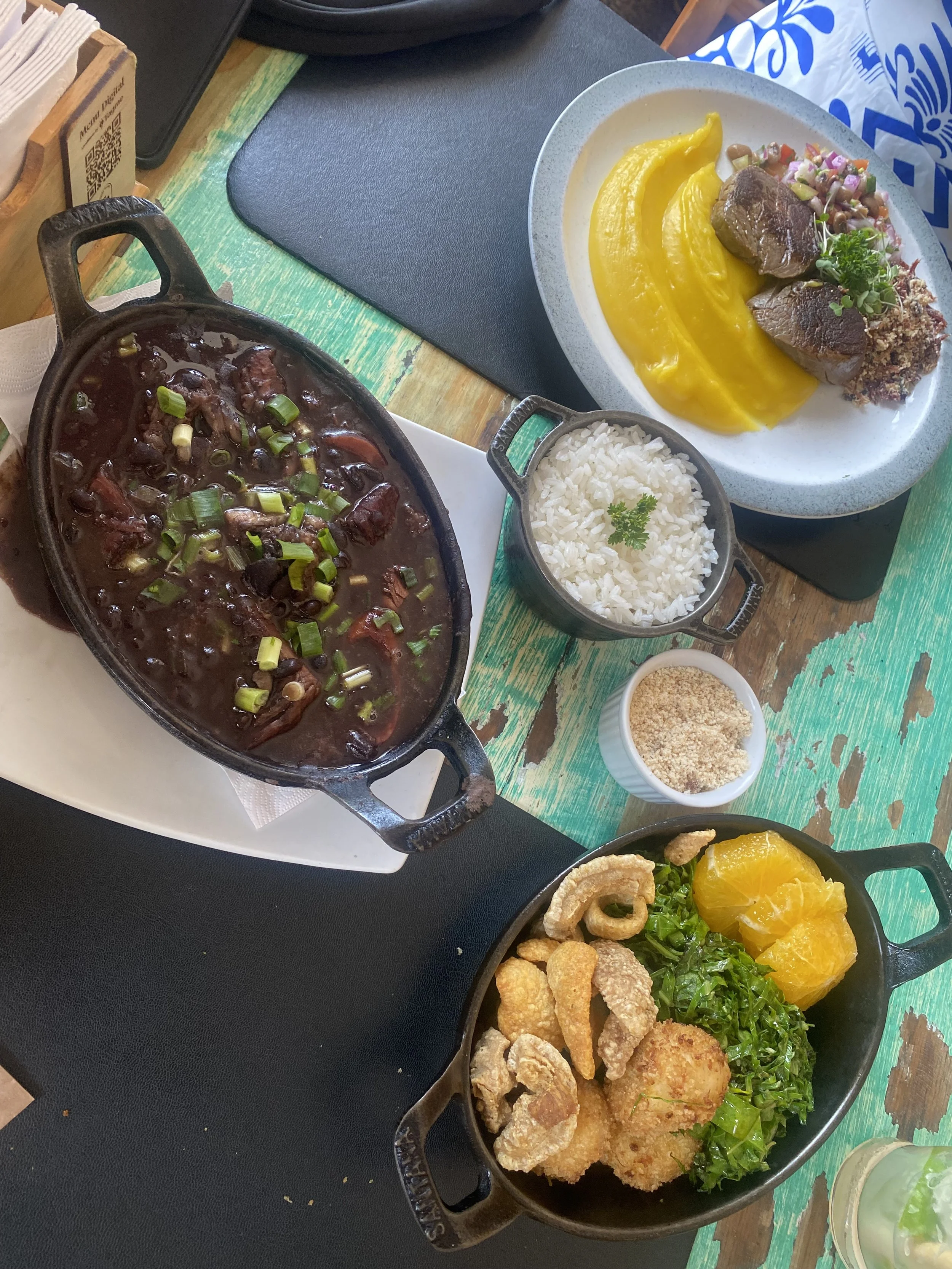 A table with various dishes of Latin American cuisine, including a spicy beef stew, rice, plantains, fried pork rinds, and stuffed peppers with yellow sauce.