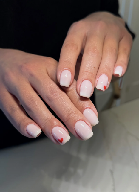 Hands with manicured nails featuring white polish and small red heart accents.