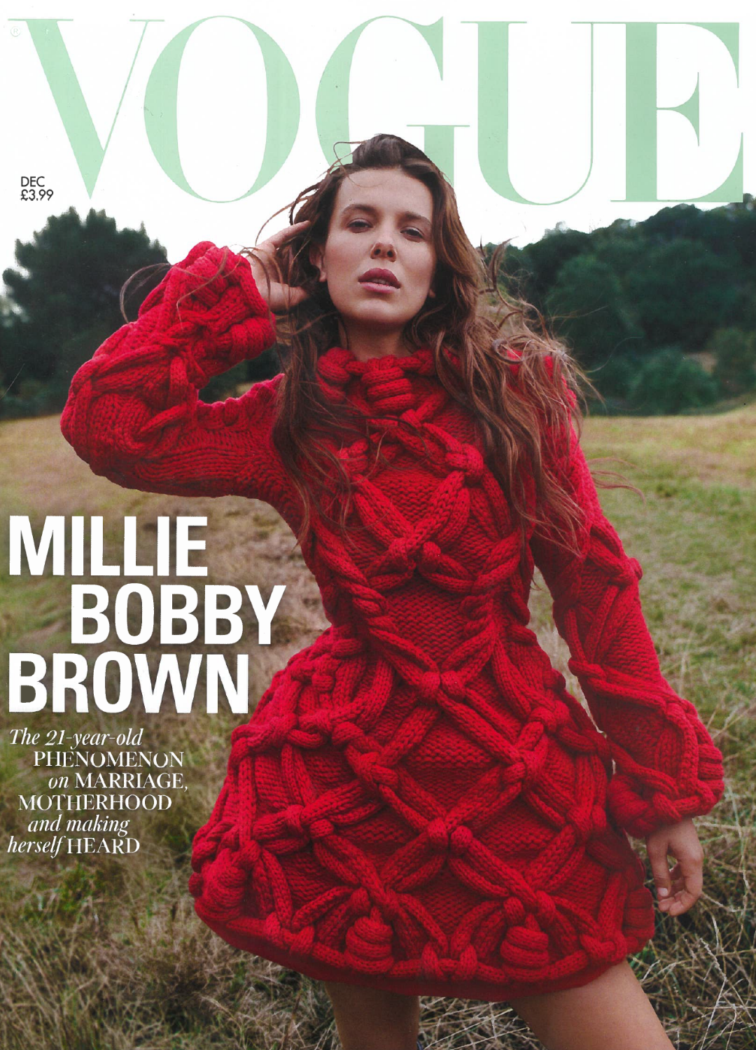 Vogue magazine cover featuring a woman (Millie Bobby Brown) with brown hair outdoors, wearing a large red, chunky knit dress with intricate patterns, set against a natural background of grass and trees.