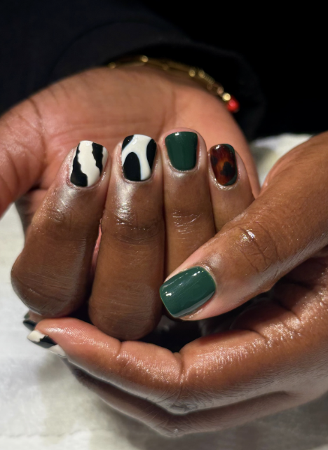Close-up of a hand with manicured nails featuring various designs, including black and white abstract print, solid green, and tortoiseshell pattern.