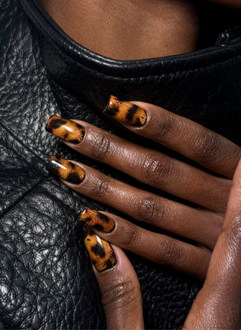 Close-up of a hand with leopard print nail art resting on a textured black leather surface.