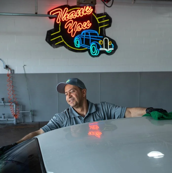 Car detailing professional at The Wash Shop hand-drying a vehicle roof with a microfiber towel.