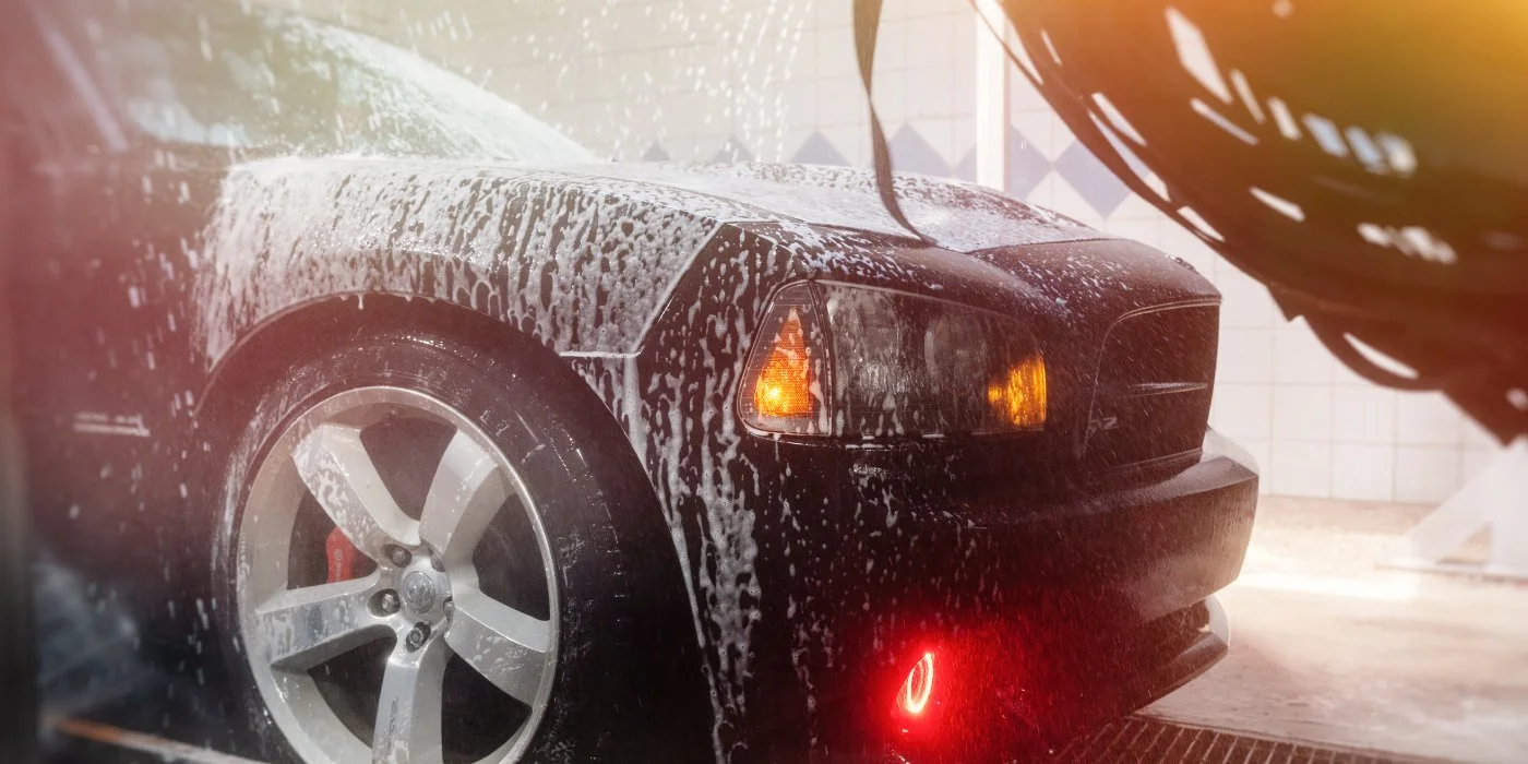 Close-up of a dark performance vehicle covered in thick soap suds during a high-quality express car wash.