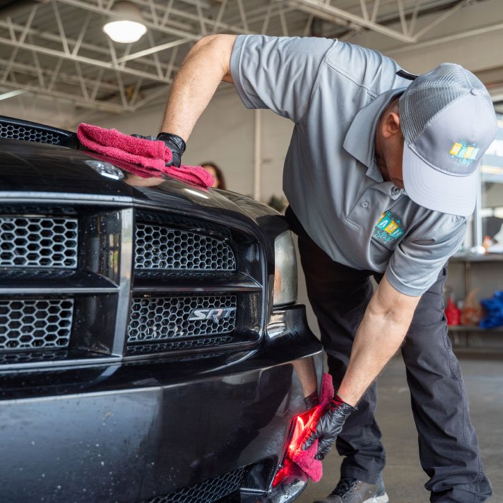 The Wash Shop auto detailing professional hand-drying the front bumper of a black Dodge SRT with a microfiber towel.