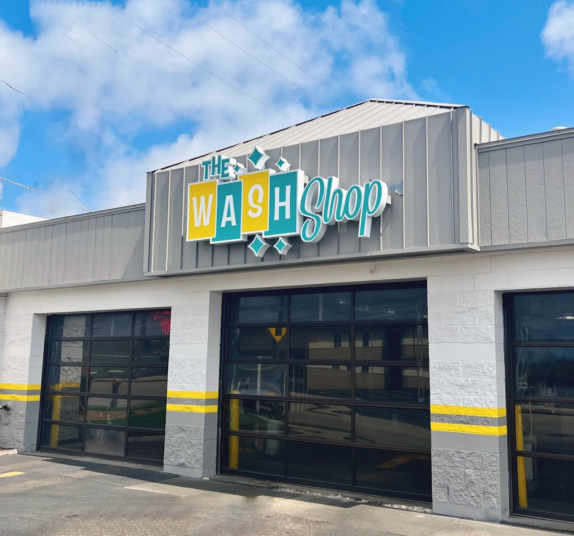 Exterior storefront of The Wash Shop featuring the teal and yellow brand sign above the car wash service bays.