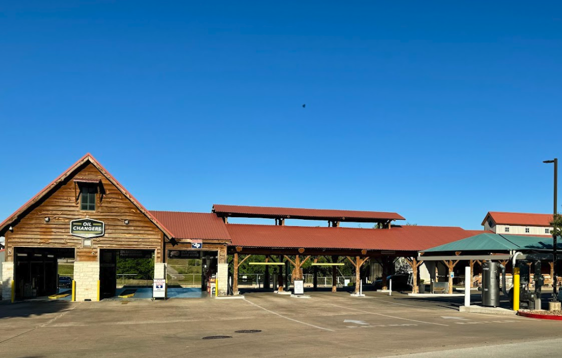 Exterior view of the rustic wood Oil Changers and The Wash Shop location, featuring drive-thru quick lube service bays.