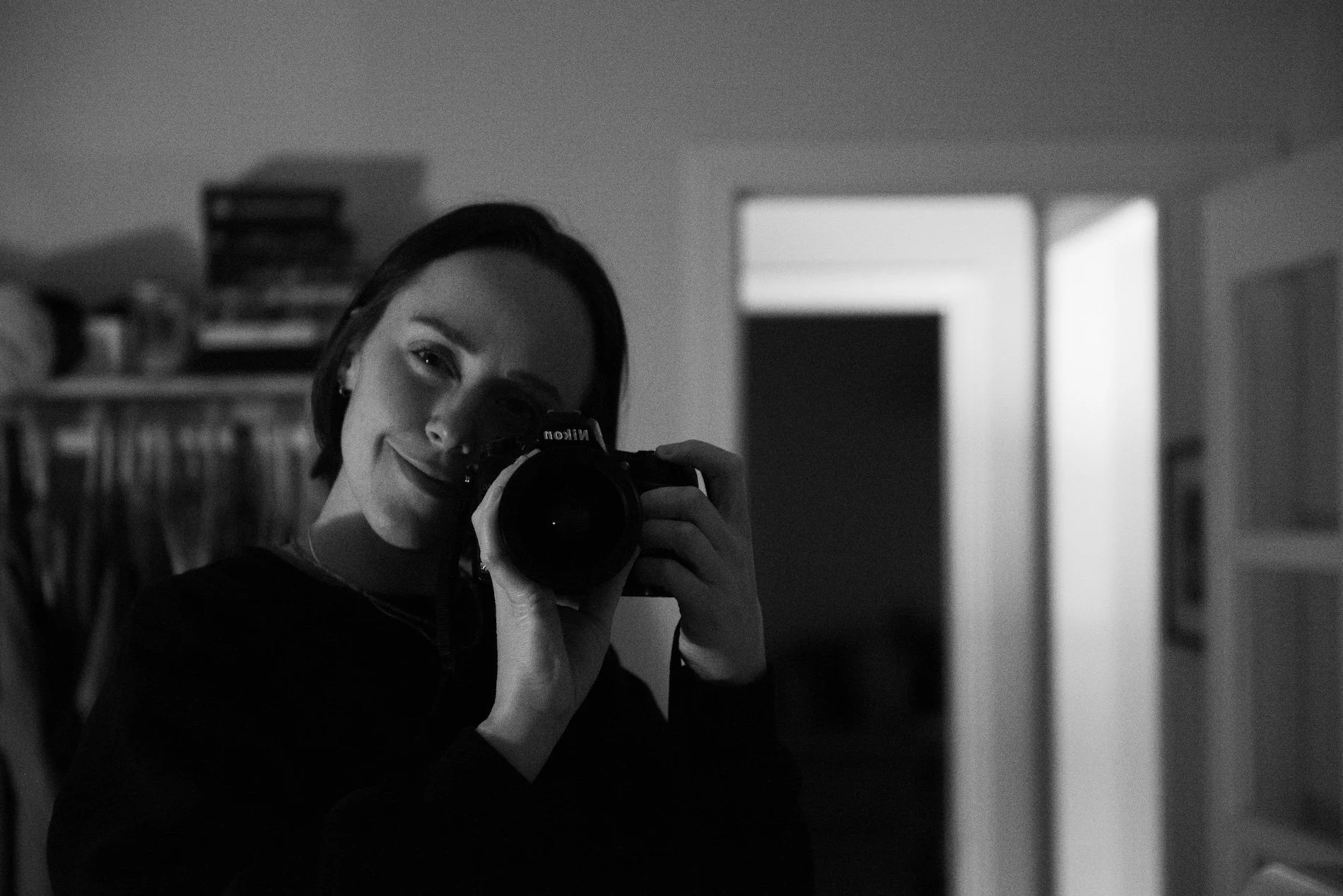 Black and white photo of a woman taking a selfie in front of a mirror with a DSLR camera.