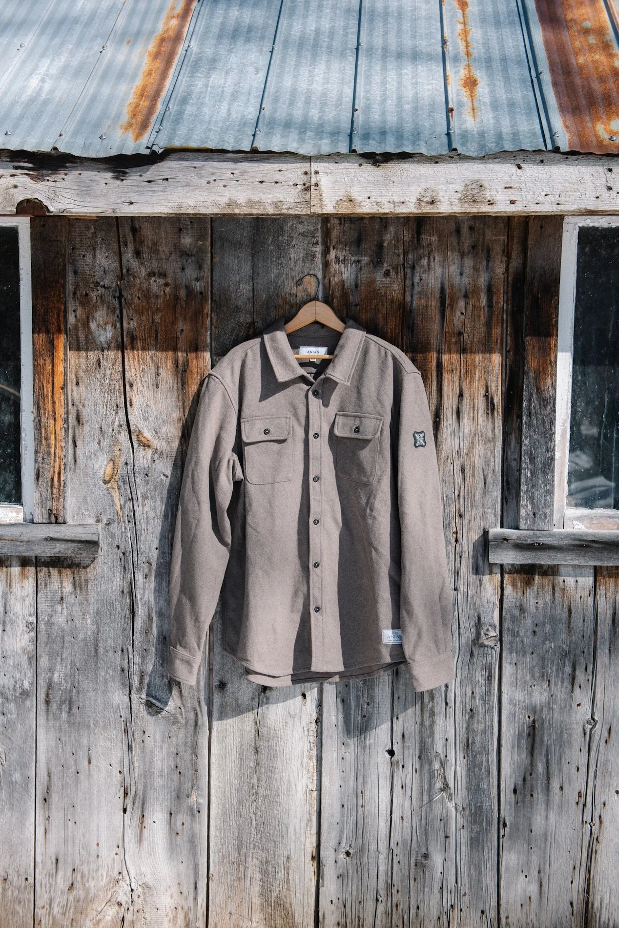 A beige button-up shirt hanging on a wooden wall outside a rustic building with weathered wood siding and small windows.