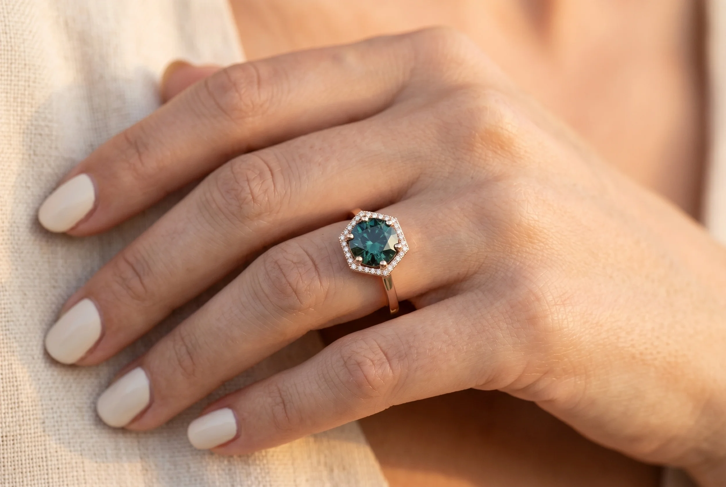 Hexagon teal sapphire engagement ring with pavé diamond halo in rose gold worn on model's hand