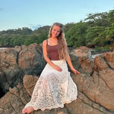 Young woman with long hair sitting on rocks outdoors with trees in the background