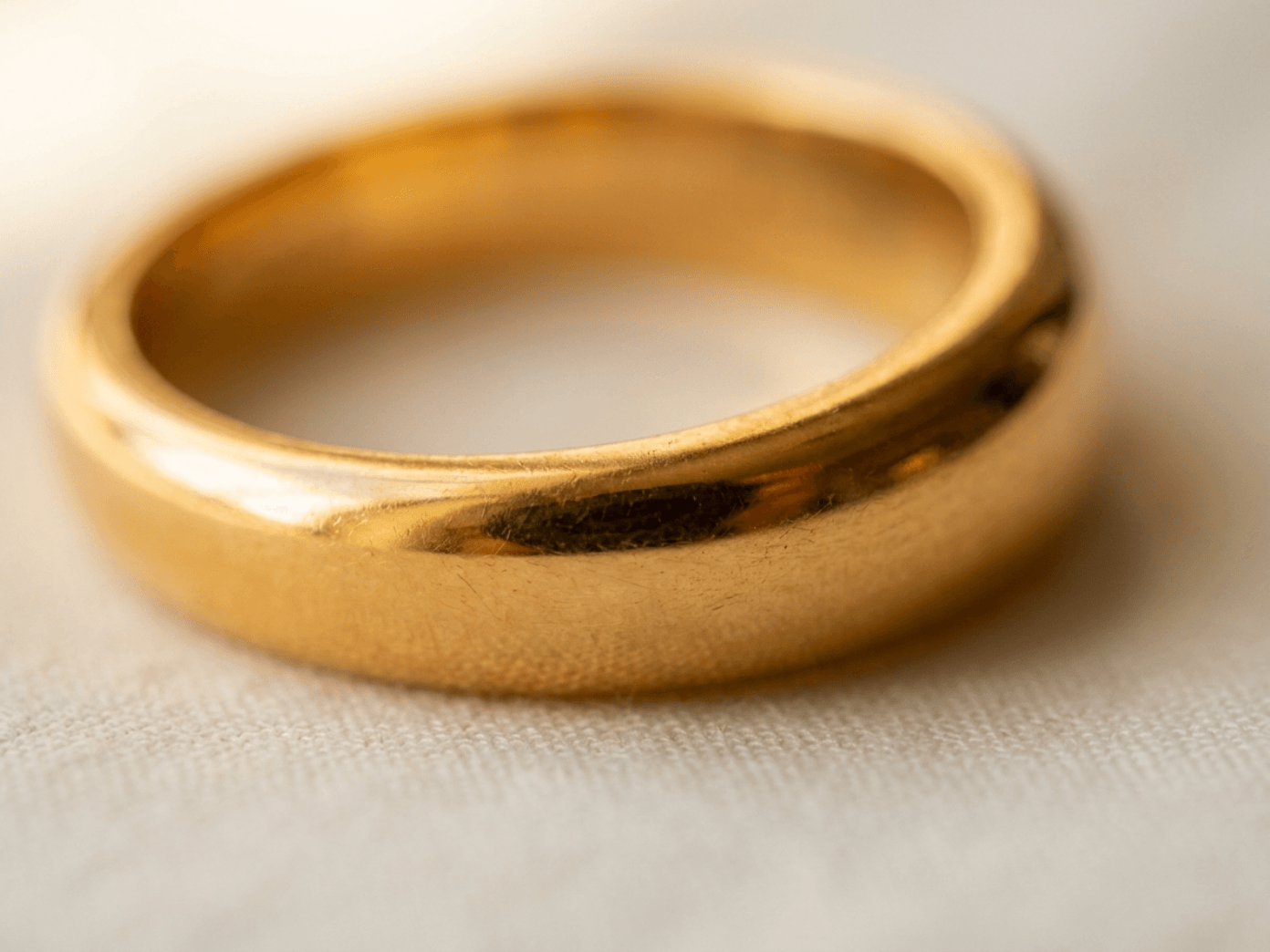 Close-up of a worn, polished yellow gold band resting on a linen surface, showing natural surface patina.