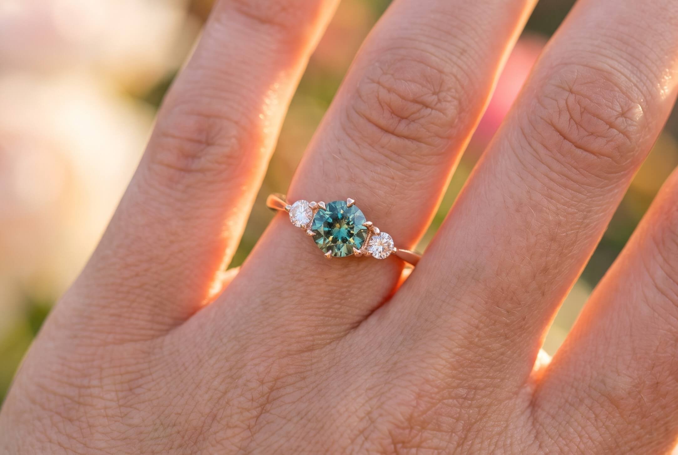 A close-up of a hand resting on a cream sweater, wearing a pear-shaped blue sapphire ring with a diamond halo.