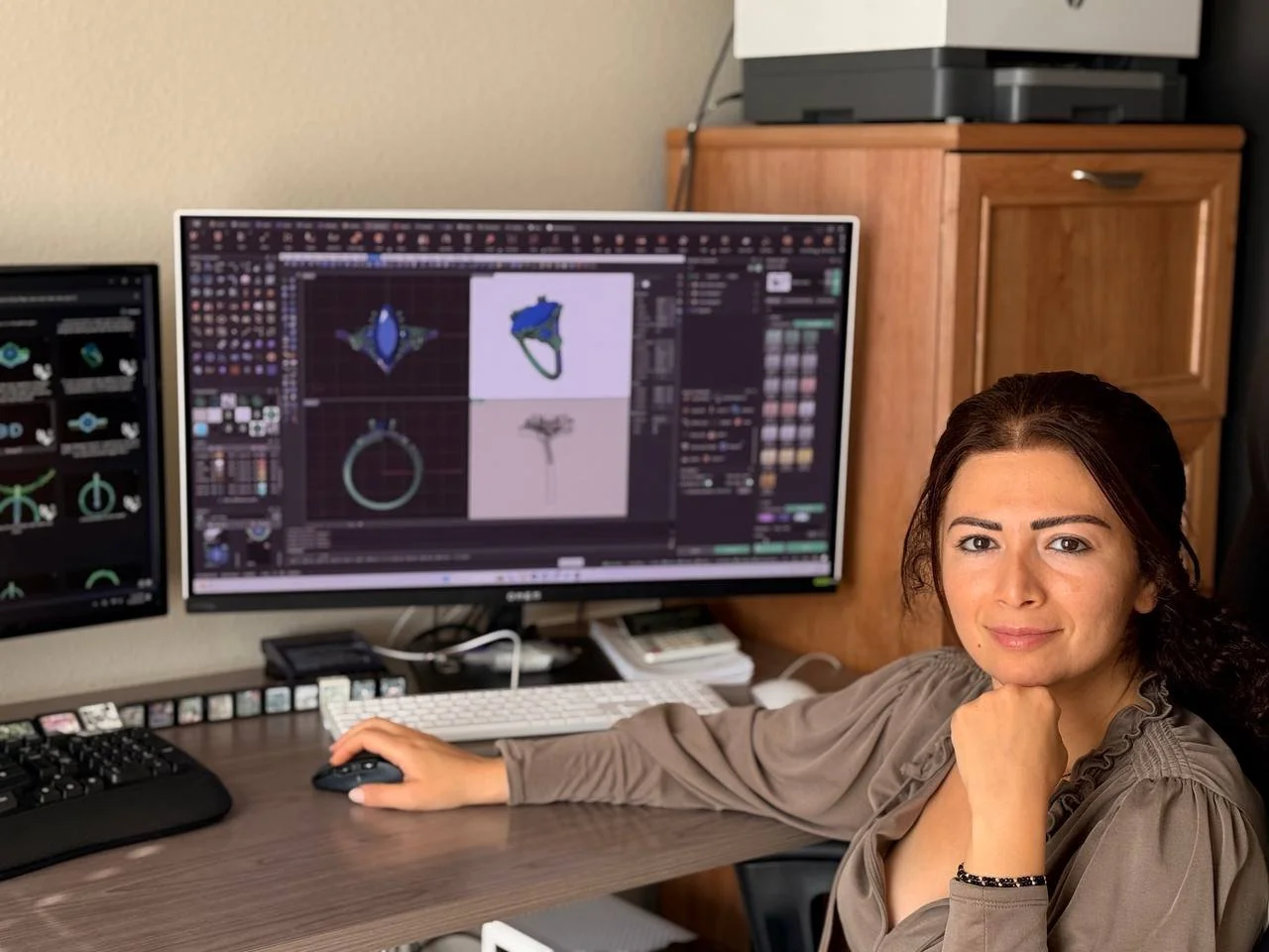 Woman working on jewelry 3D modeling at a computer with multiple monitors displaying jewelry renderings.