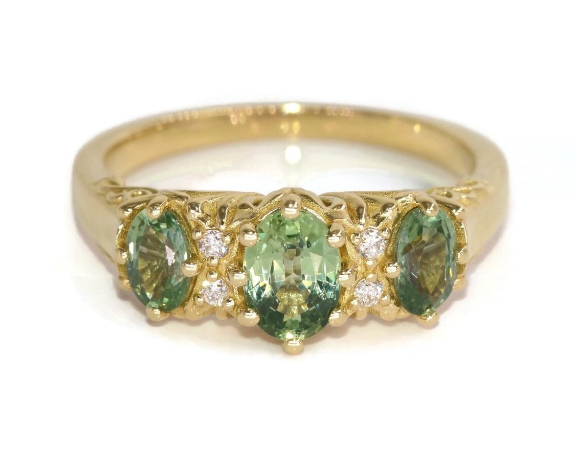 Oval green sapphire three-stone engagement ring with diamond accents and filigree setting in yellow gold, front view