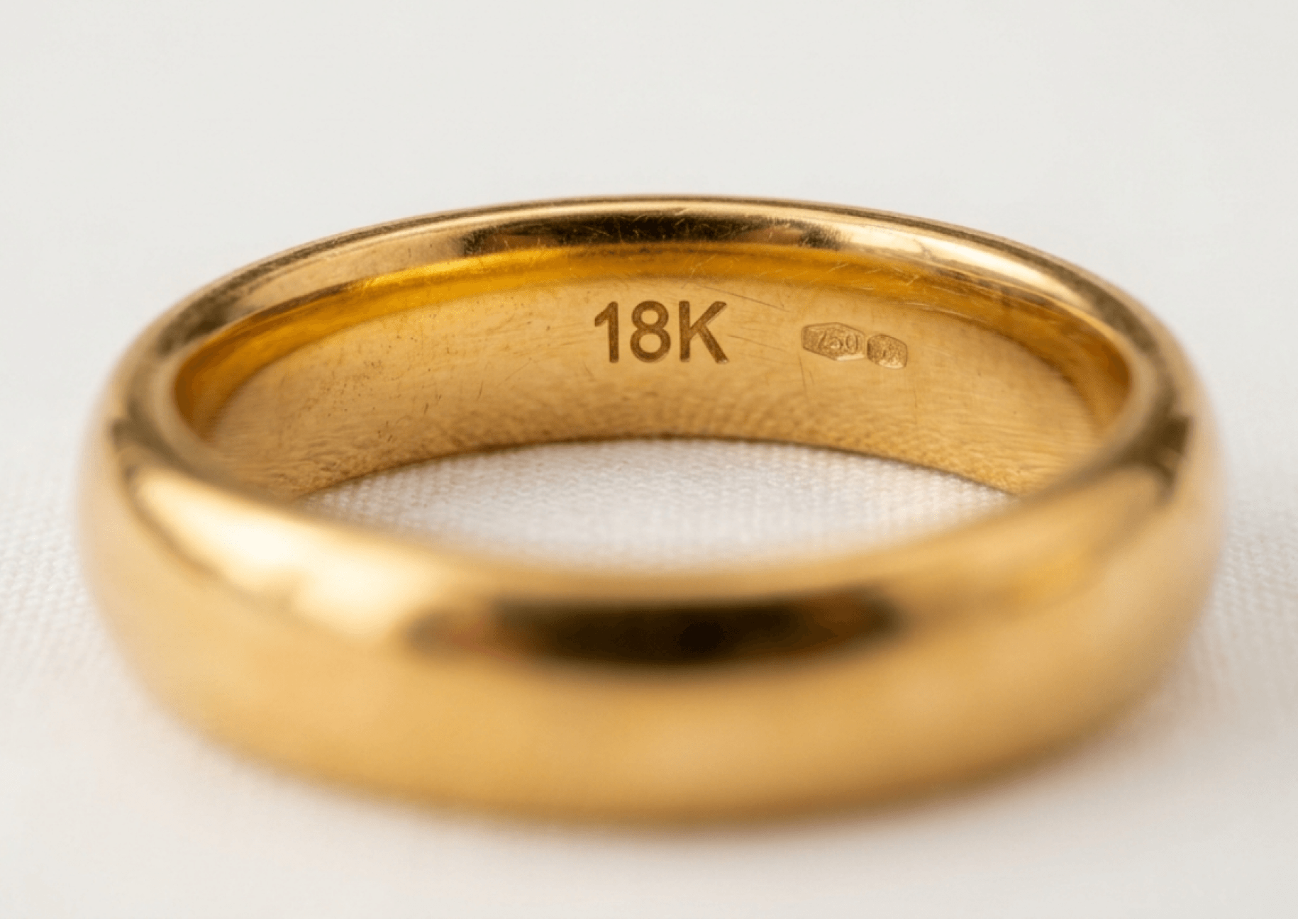 Close-up of the inside of a polished gold band showing an engraved '18K' hallmark and a 750 stamp.