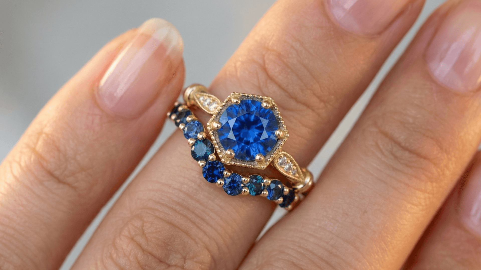 Close-up of a hand showing two gold rings with blue gemstones on the ring finger.