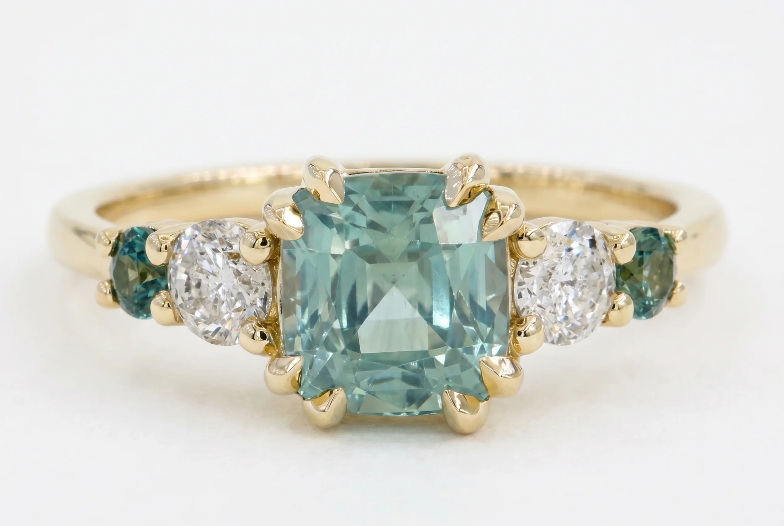 Asscher cut teal sapphire five-stone engagement ring with oval diamond and teal sapphire accents in yellow gold