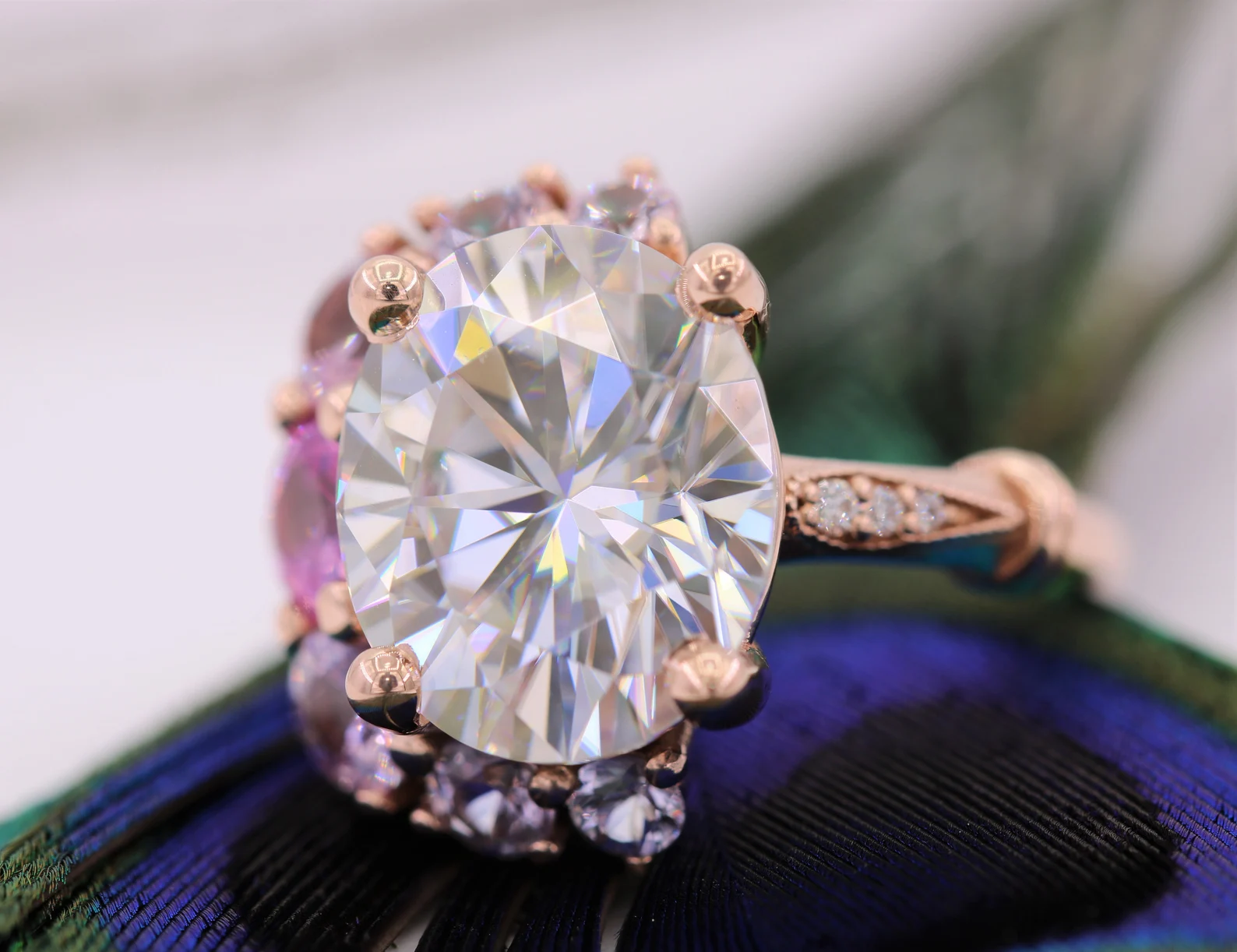 Close-up of an ornate ring with a large, oval-shaped diamond surrounded by smaller diamonds, set in a rose gold band, resting on a peacock feather.