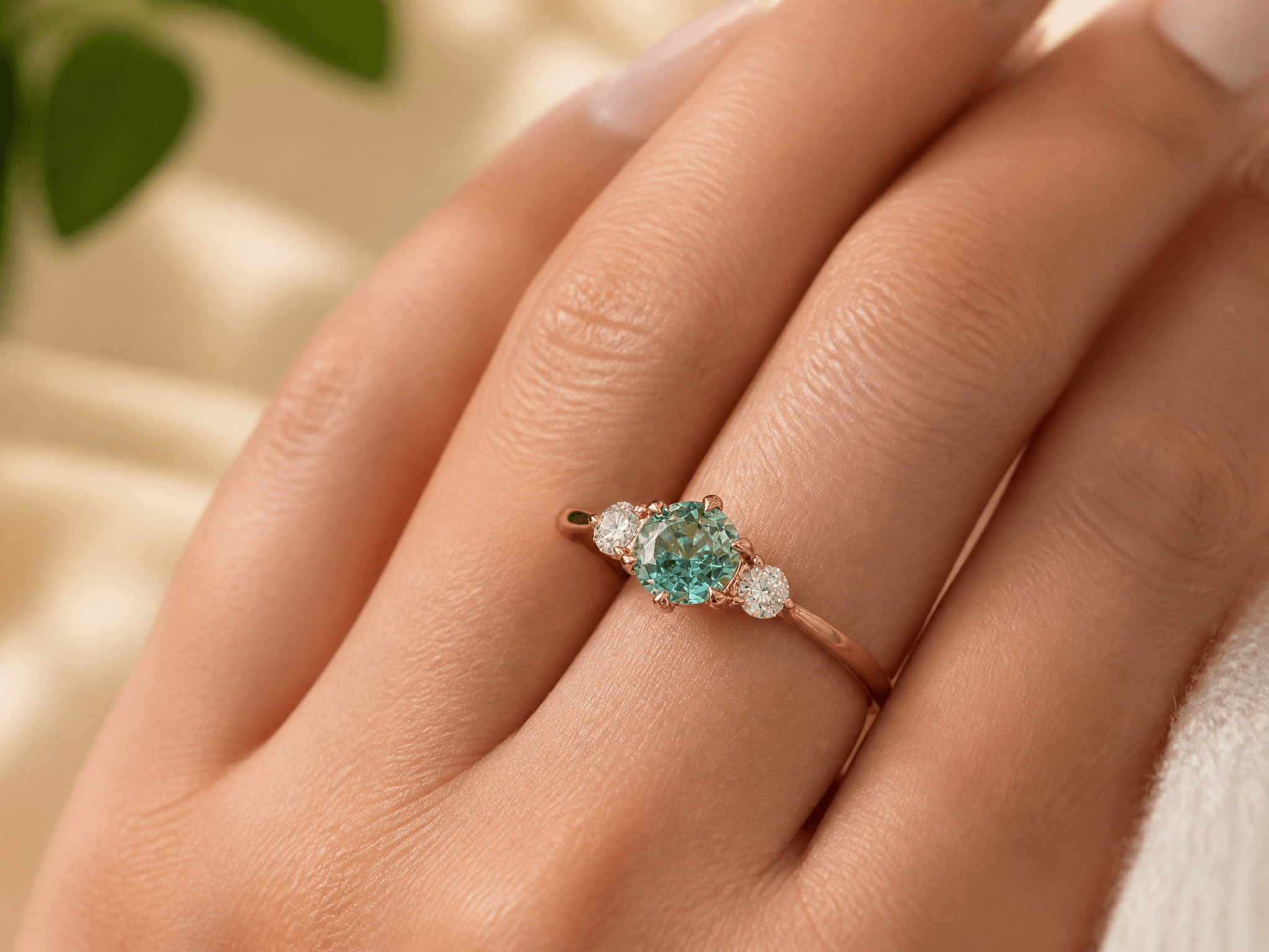 A close-up of a hand wearing a delicate three-stone ring with a round mint green center gemstone flanked by two small diamonds on a thin gold band.