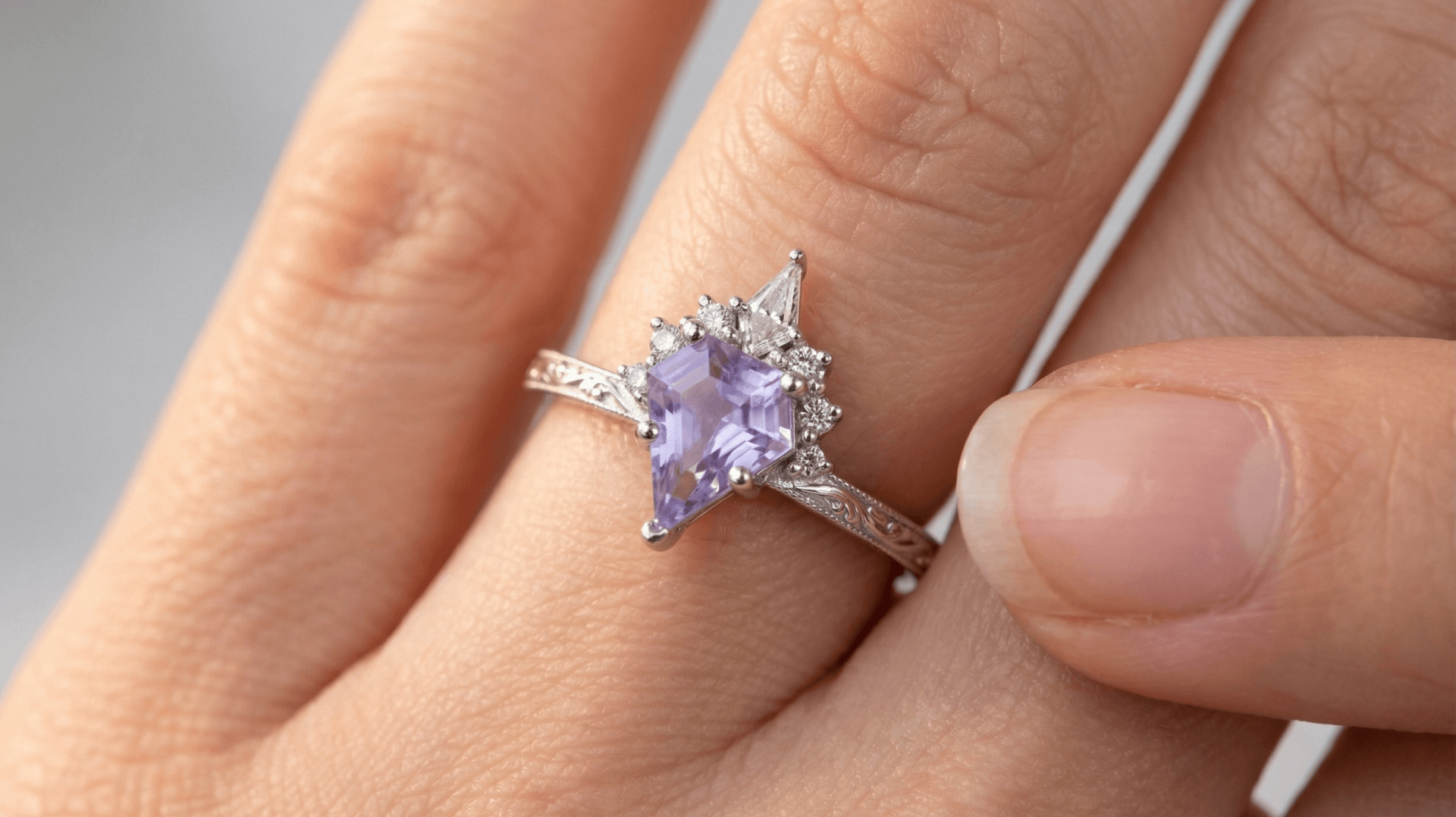 A close-up of a hand wearing a silver ring with an oval purple gemstone surrounded by small diamonds, on a finger.