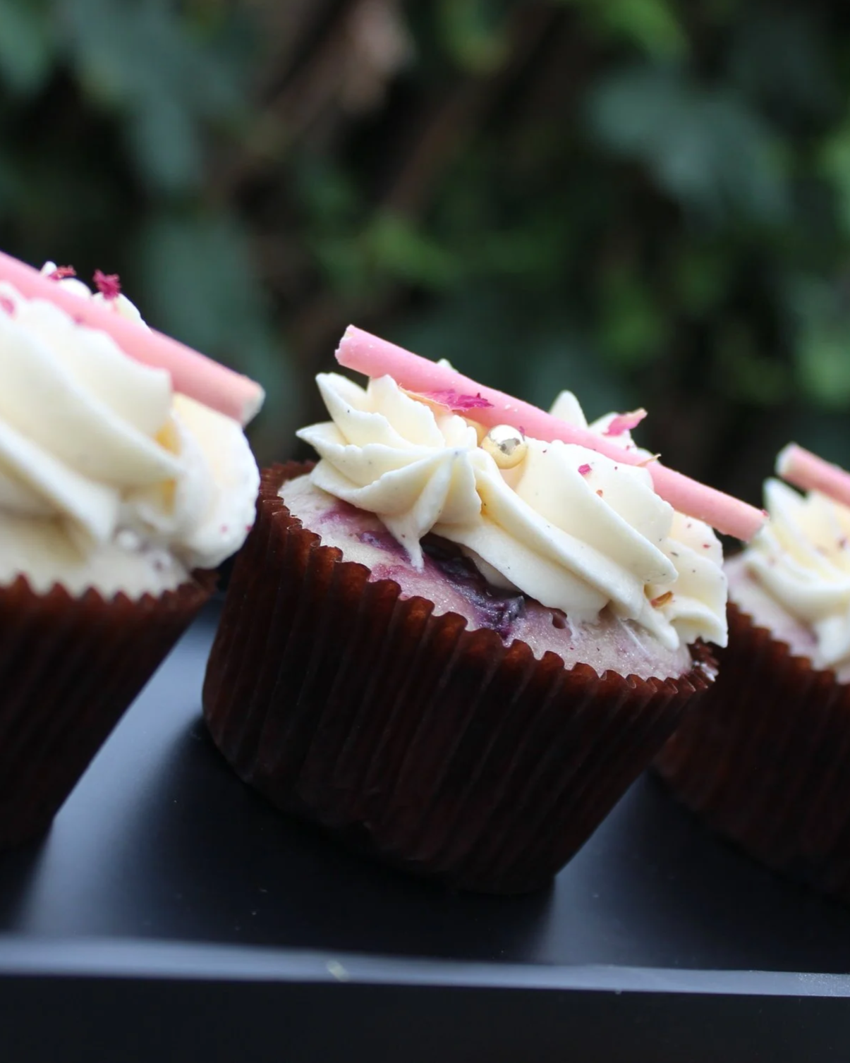 Love Spell: A soft mixed-berry and vanilla bean cupcake swirled with vanilla bourbon buttercream, topped with a white chocolate dipped cookie stick.