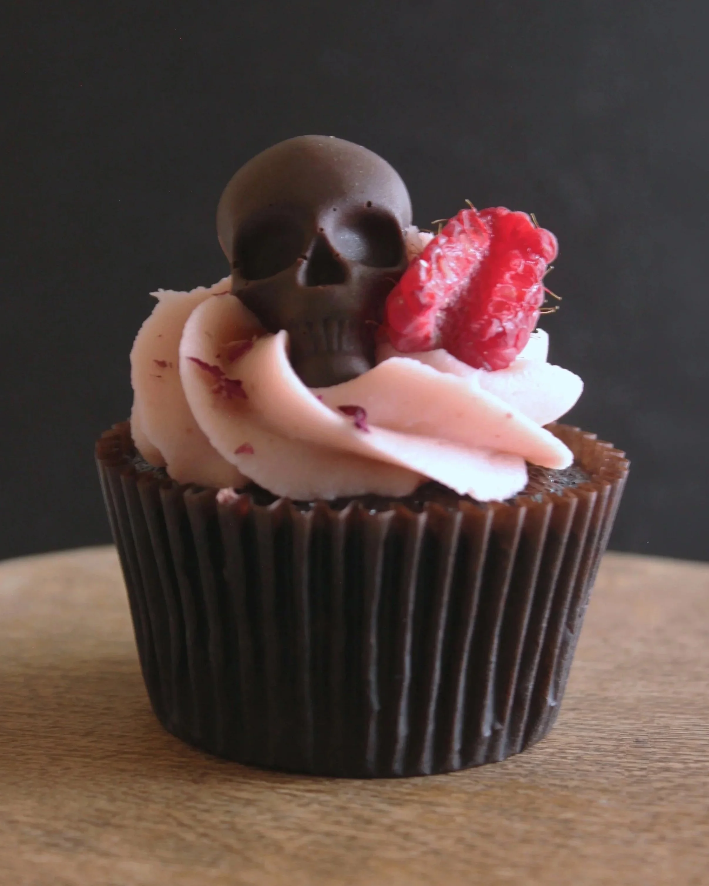 Blaque Velvet: A striking black-dyed red velvet cupcake layered with tangy raspberry cream cheese buttercream, and topped with a chocolate skull and a raspberry.