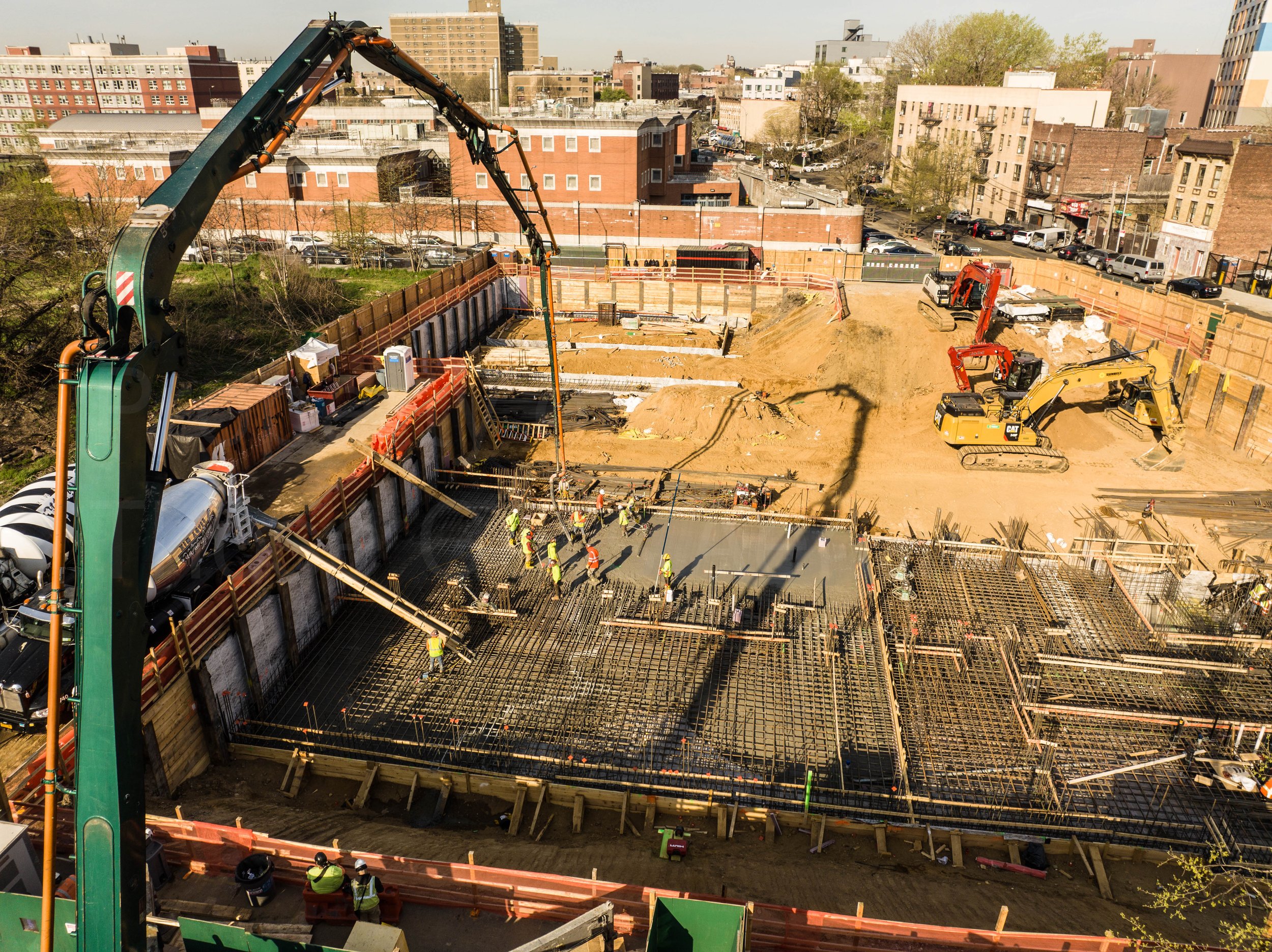 Construction site with workers and machinery, including a large cement truck and excavators, in an urban area, at 326 Rockaway Ave. Brownsville - Brooklyn