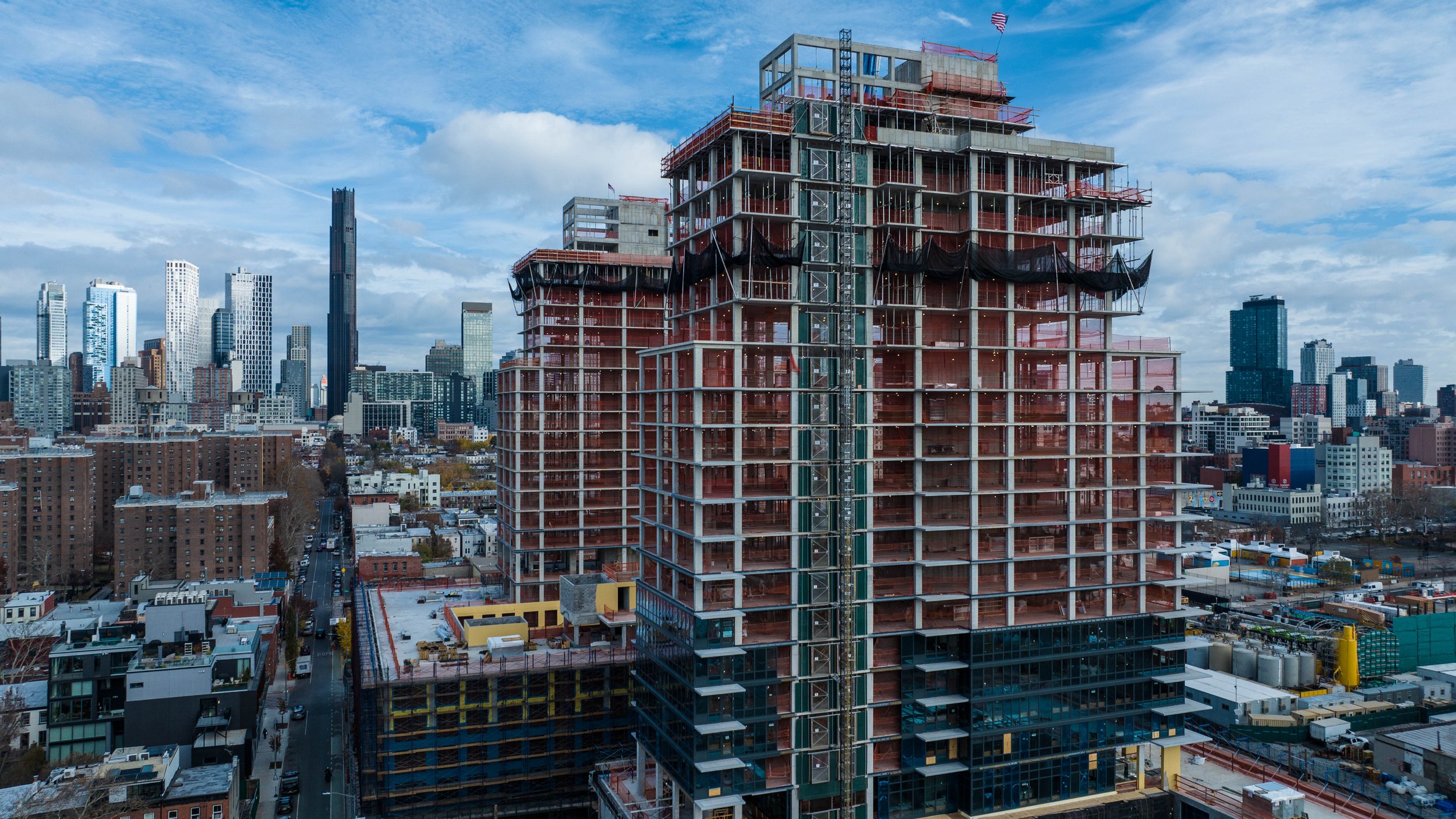 A tall building under construction in the Gowanus area city skyline, with a background of modern skyscrapers and a partly cloudy sky.