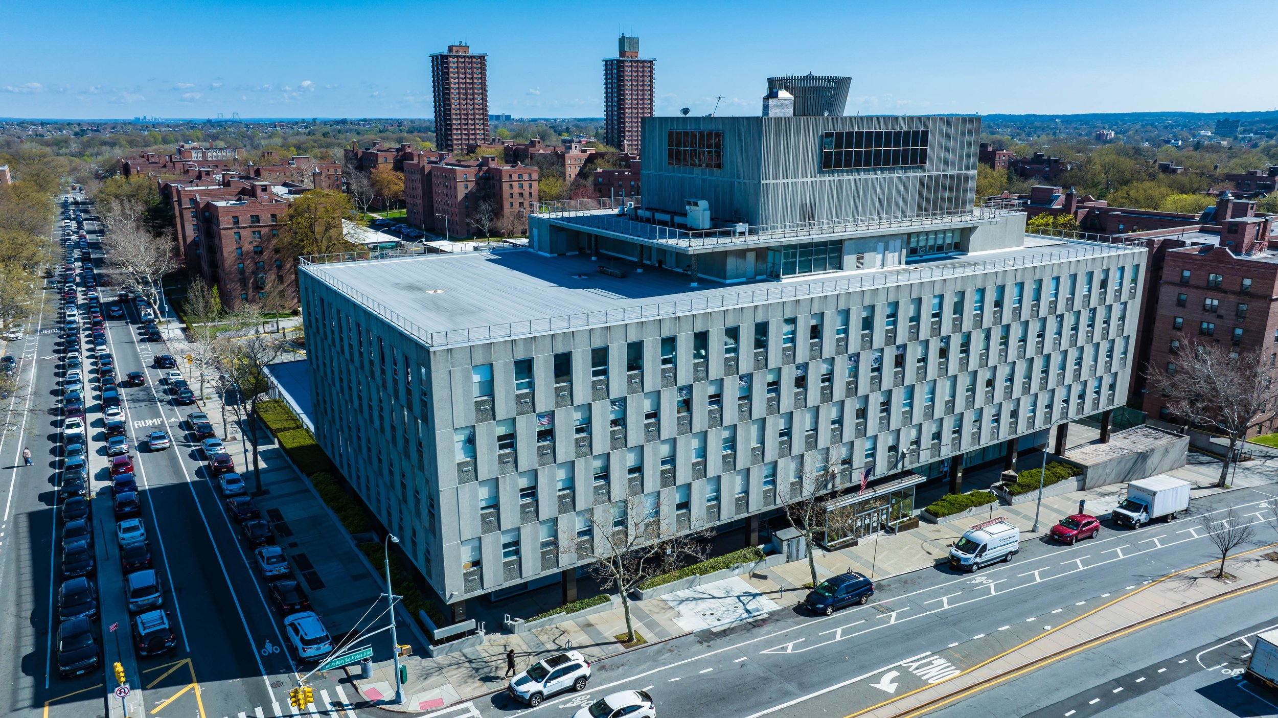 Aerial view of a modern multi-story office building, "Local Union #3 IBEW Joint Industry Board" electrical workers union with a unique design, surrounded by streets and cars, with residential buildings and trees in the background.