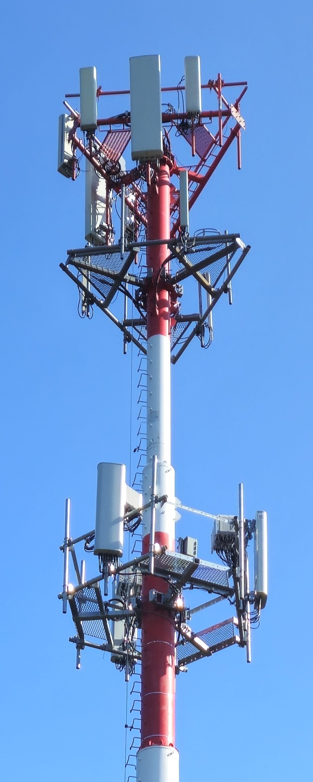 Telecommunications tower with multiple antennas and equipment against a clear blue sky.