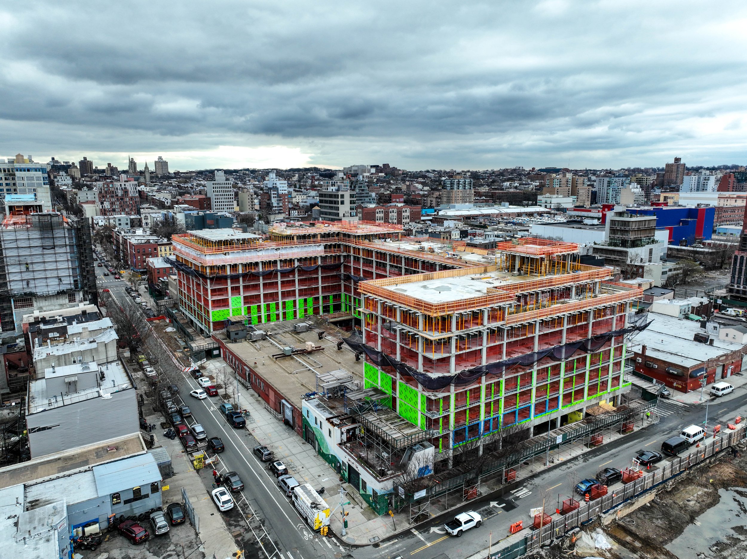Aerial view of a large multi-story building along the Gowanus Canal under construction in an urban area, with surrounding buildings and streets visible.