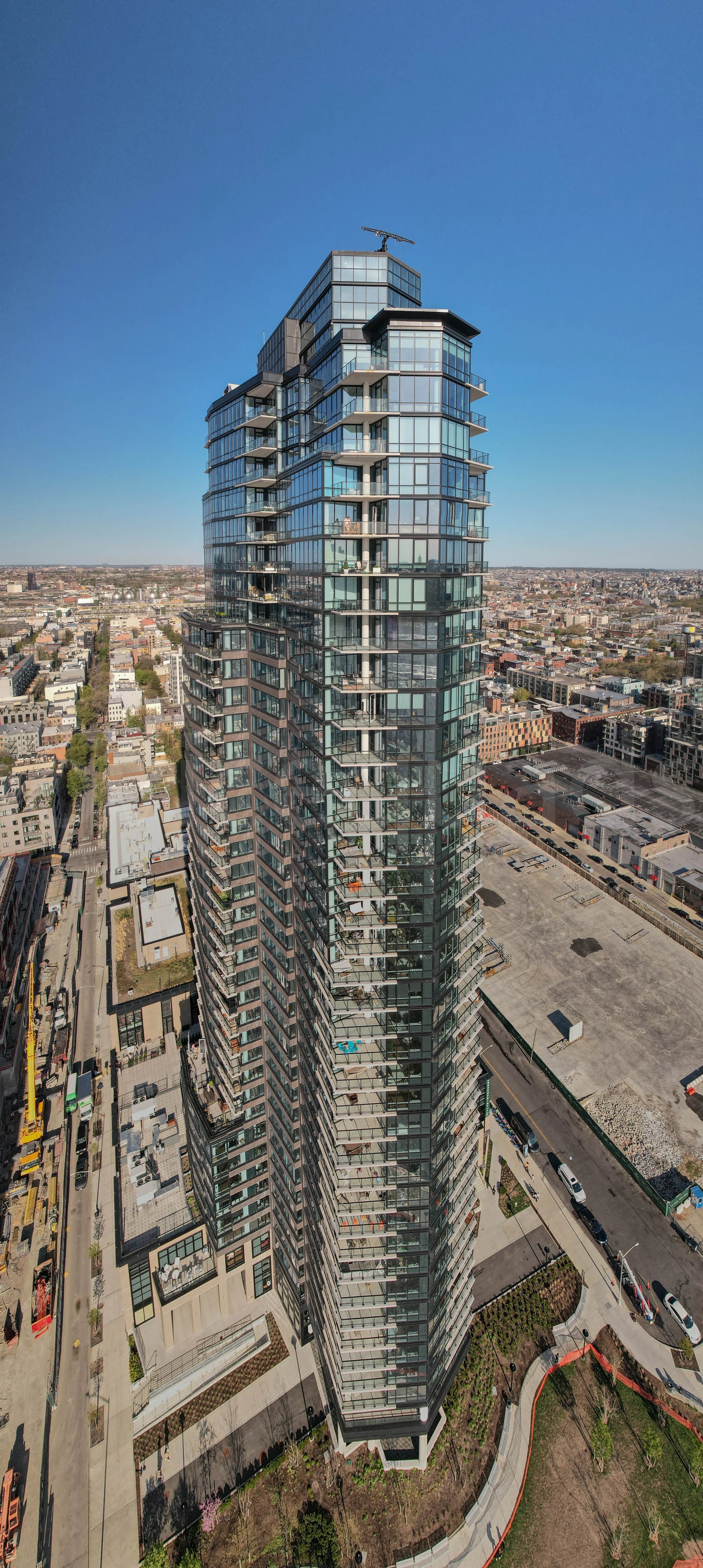Simmerce Commerce building is a tall modern glass skyscraper with multiple balconies on each floor, set against a clear blue sky in an urban area, Brooklyn
