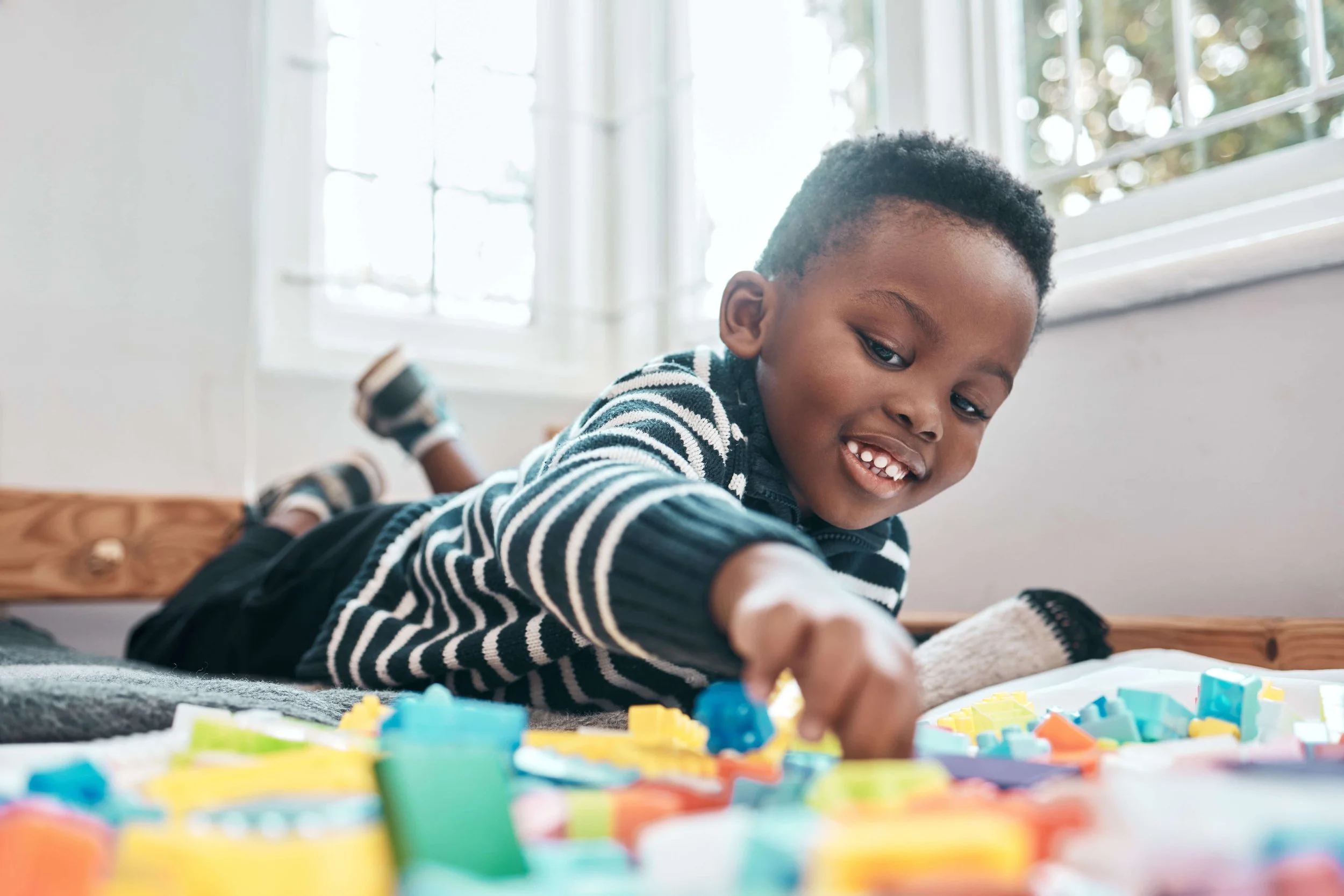 Young boy lying on his stomach playing with colorful board game pieces during in-home speech therapy for kids in Zebulon, NC.