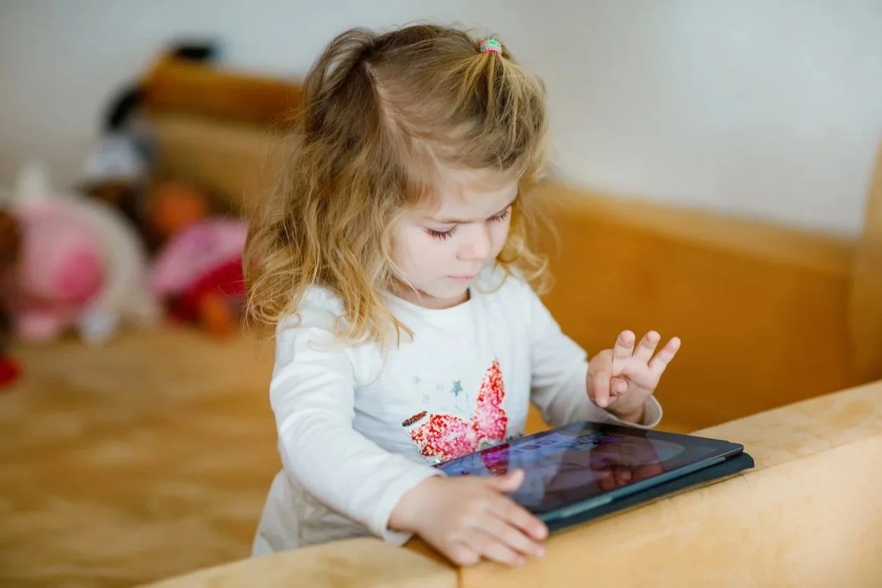 A young girl with curly hair and a ponytail, sitting at a wooden table working on using an AAC app to communicate during AAC therapy for kids in Zebulon, NC.