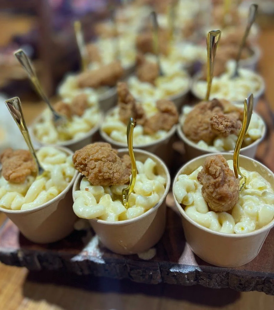Cups of macaroni and cheese topped with fried chicken bites and gold-colored forks.