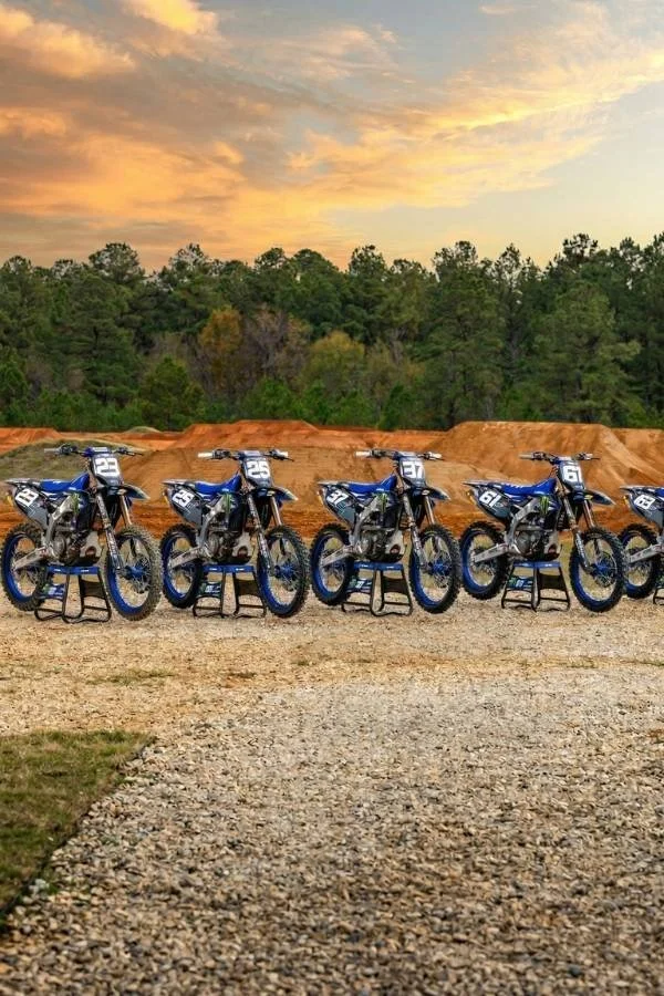 Motocross dirt bikes lined up on a gravel track beneath a sunset sky.