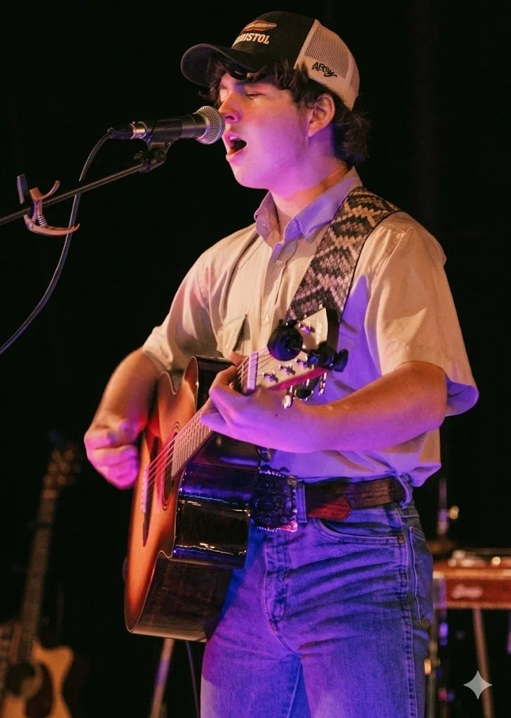 Man performing music on stage, playing an acoustic guitar.