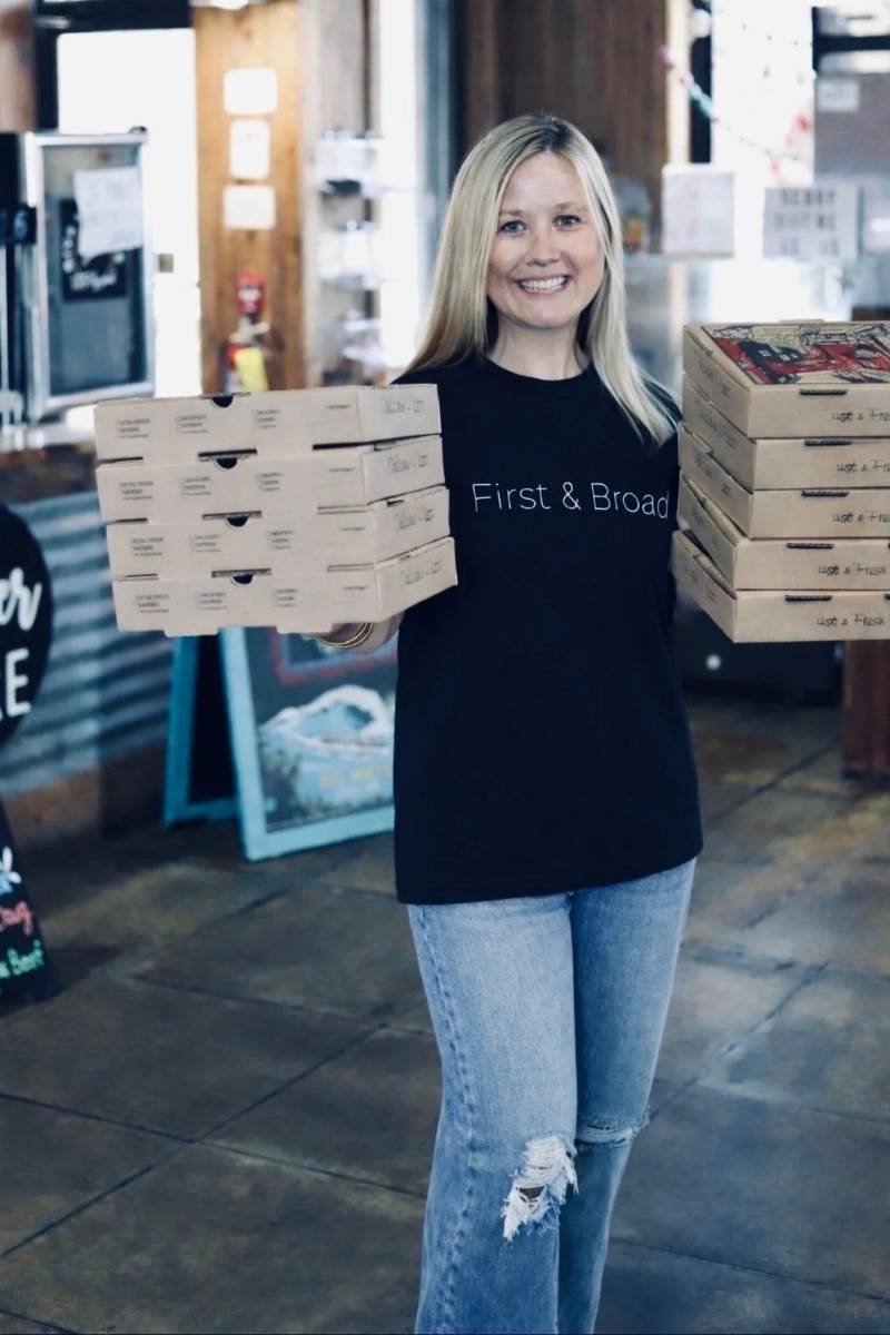 Restaurant owner holding stacked pizza boxes for pickup or delivery orders.