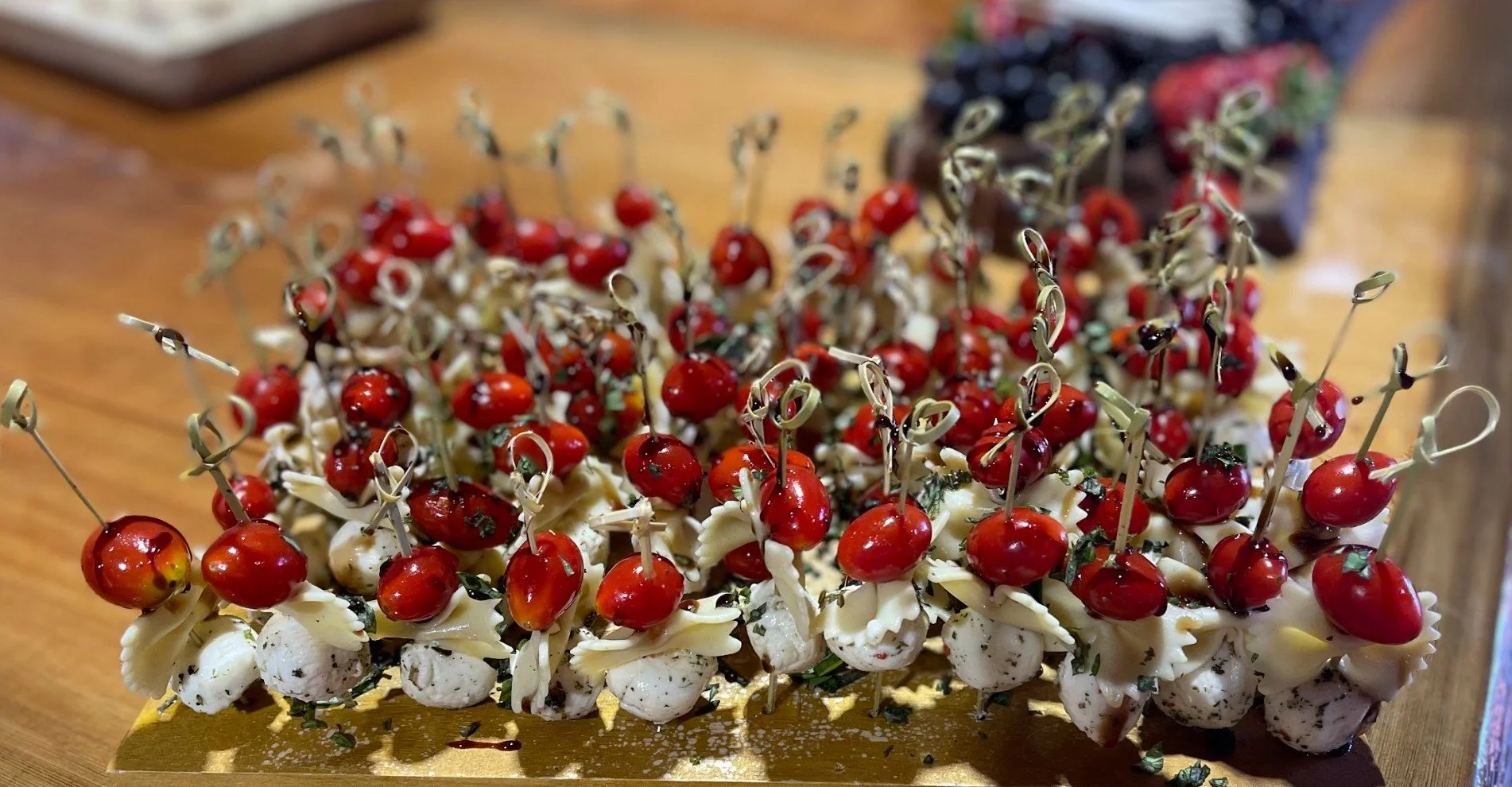 Appetizer platter with cherry tomatoes, mozzarella balls, and herbs on skewers, arranged on a gold-colored tray.