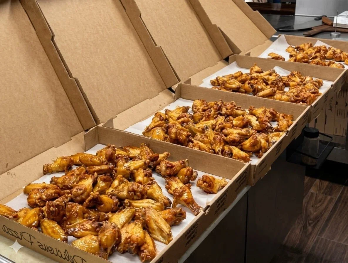 Four open cardboard boxes filled with cooked chicken wings on a table.