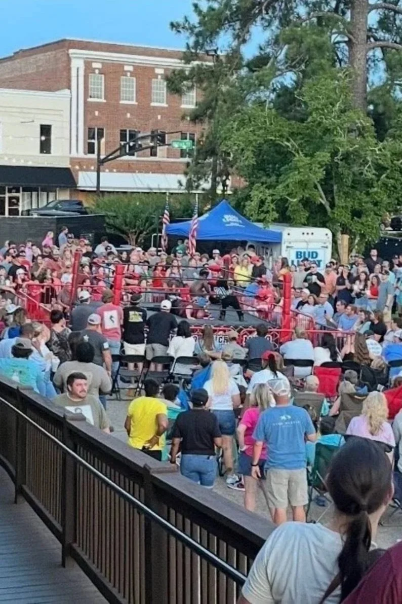 Large outdoor community event with guests gathered around a boxing ring.