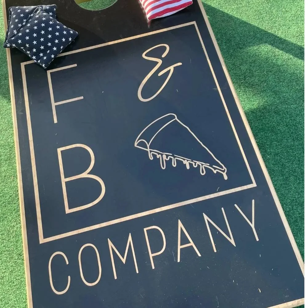 First and Broad Pizza Company cornhole board with bean bags on outdoor turf.