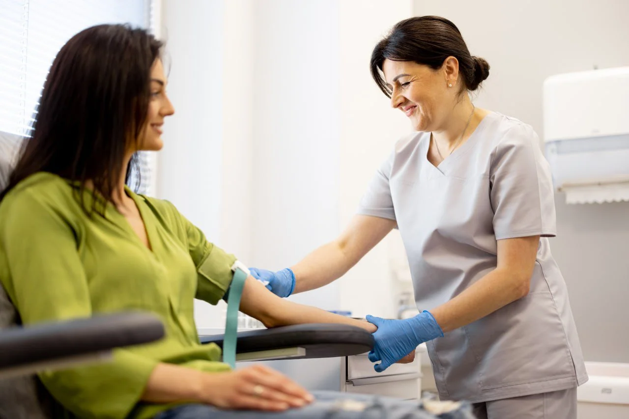 Nurse drawing blood from a smiling woman patient in a medical office.