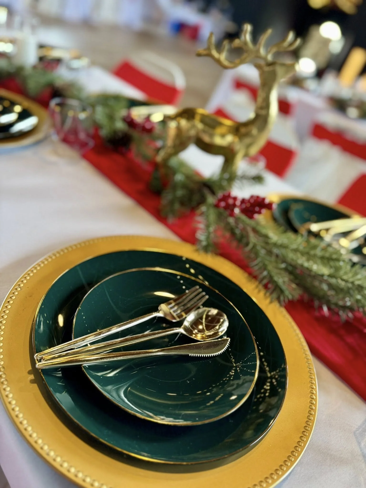 Elegant Christmas dinner table setting with gold, green, and red themed dishes and decorations, including a gold reindeer centerpiece and festive greenery.