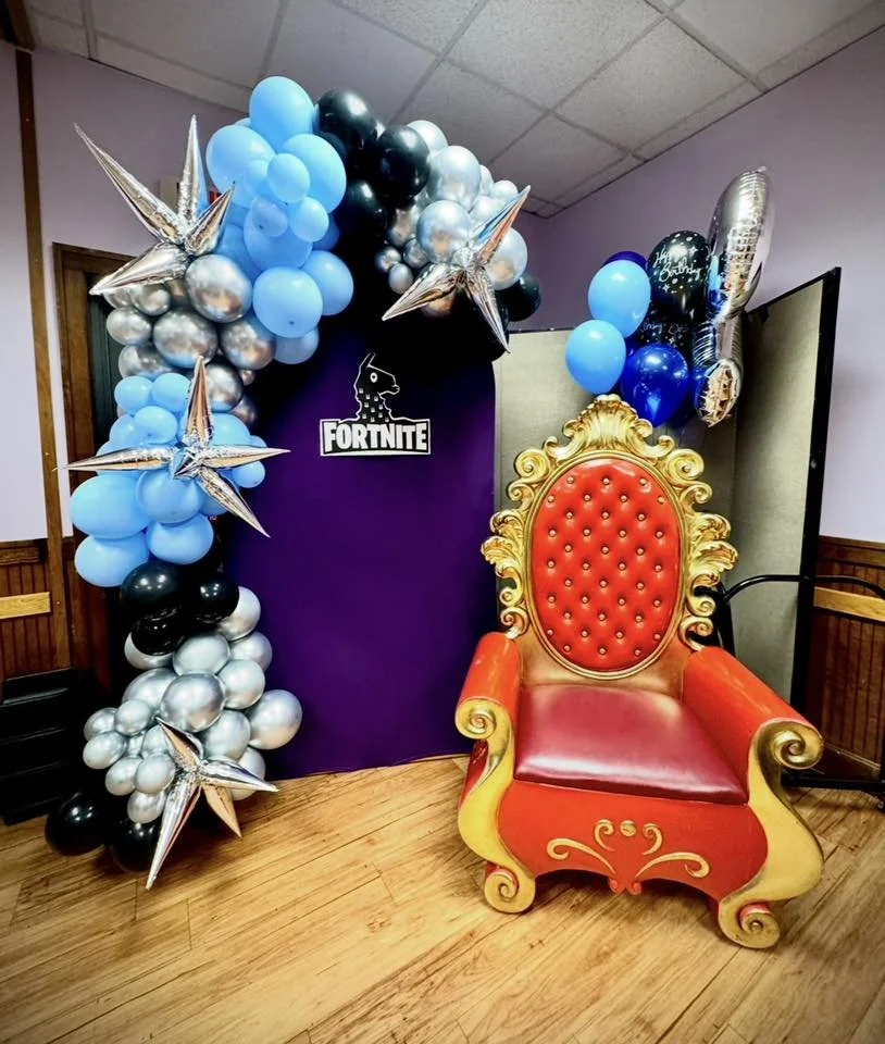Decorative Fortnite-themed balloon arch with star-shaped balloons, and a red and gold throne for a birthday celebration.