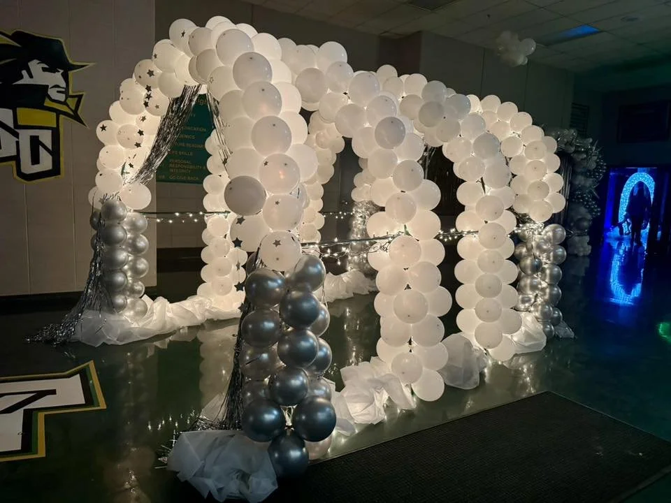 White and silver balloon arch decoration with fairy lights, set up indoors for an event.