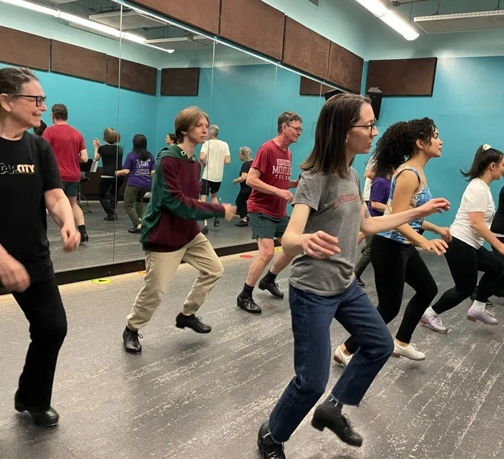 Group of people participating in a dance or exercise class in a studio with mirrored walls and blue walls.