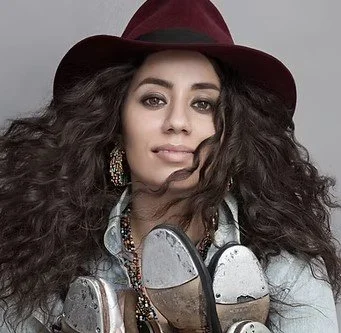 Portrait of a woman with curly hair wearing a maroon hat and large earrings, holding a golf club.