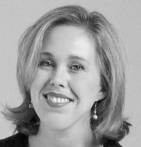Black and white photo of a woman smiling, wearing earrings and a dark top.