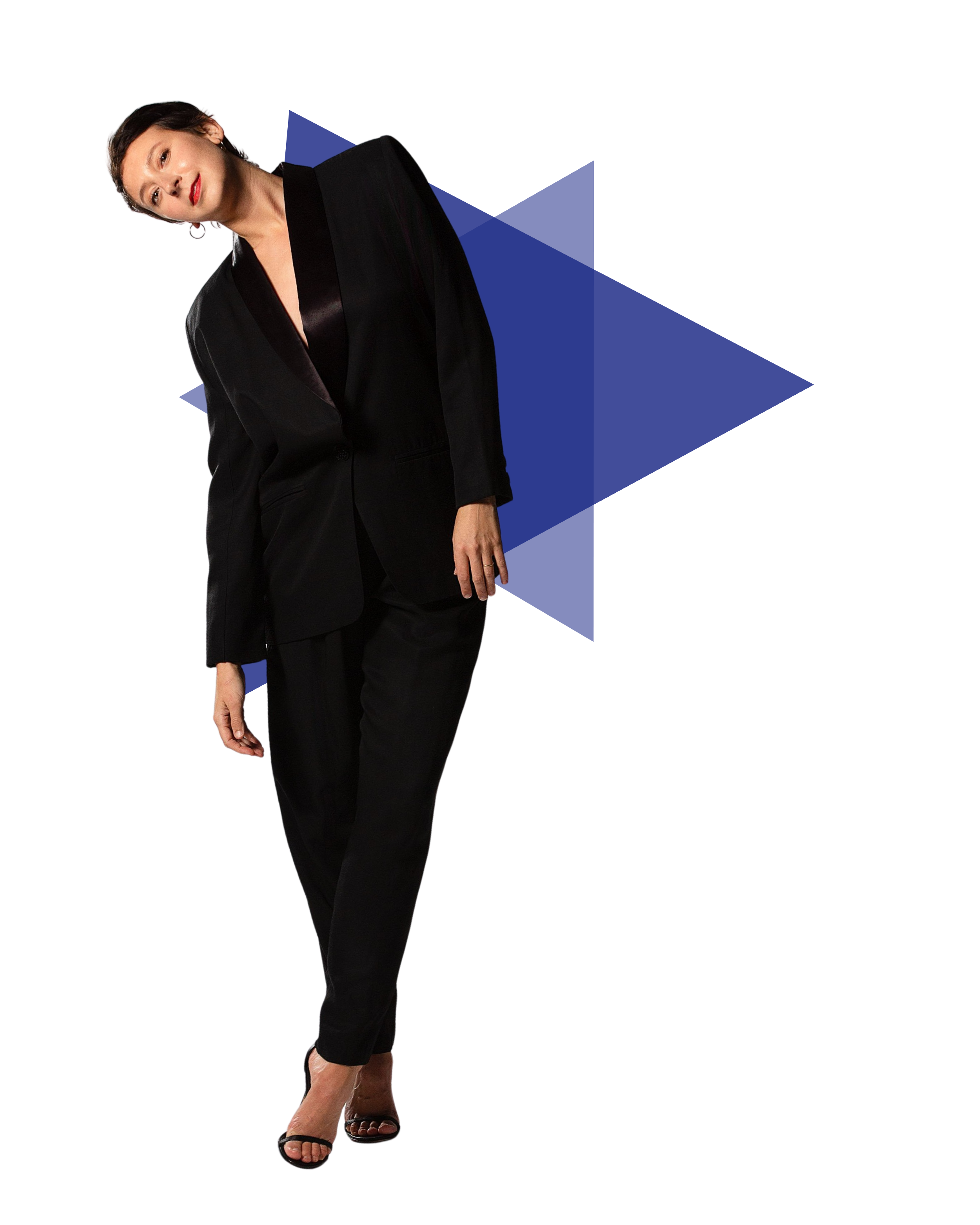 A woman dressed in a black suit with an oversized blazer, standing and leaning slightly to the left, against a background of colorful, abstract geometric shapes.